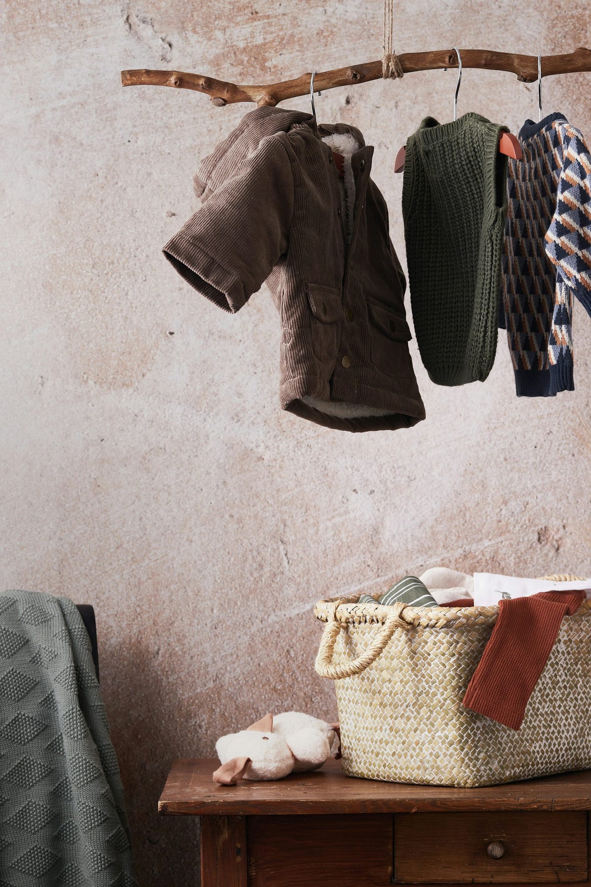 Children's knitwear hanging from a wooden branch above a basket